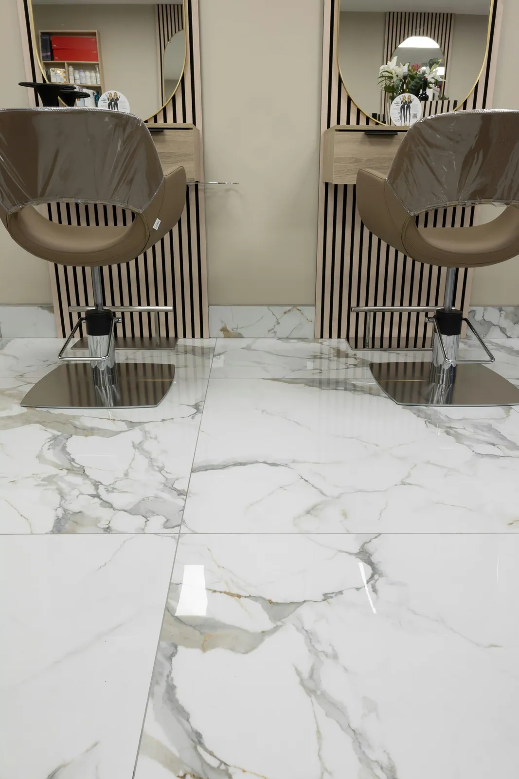 Two taupe styling chairs reflected on a glossy white floor with broad gray and warm beige veining.